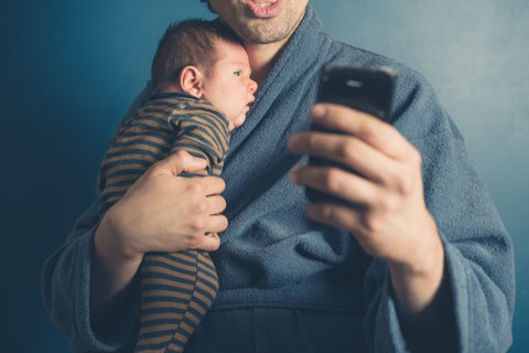 man holding baby while looking at cell phone