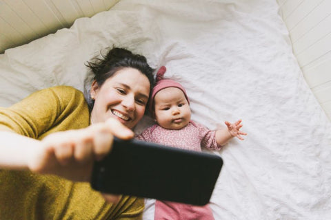 woman and baby looking up at smartphone lying on the bed