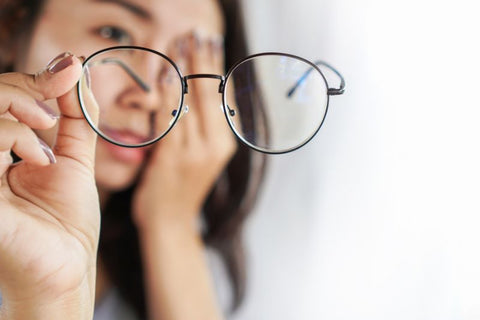 a woman holding a pair of glasses and rubbing her eye