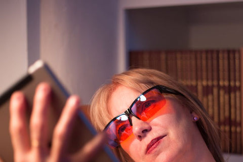 woman looks at tablet with orange lens glasses on to ensure she keeps to her recommended screen time by age