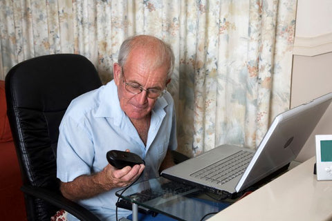 senior man sat at computer holding up mouse to look at it for recommendations on screen time