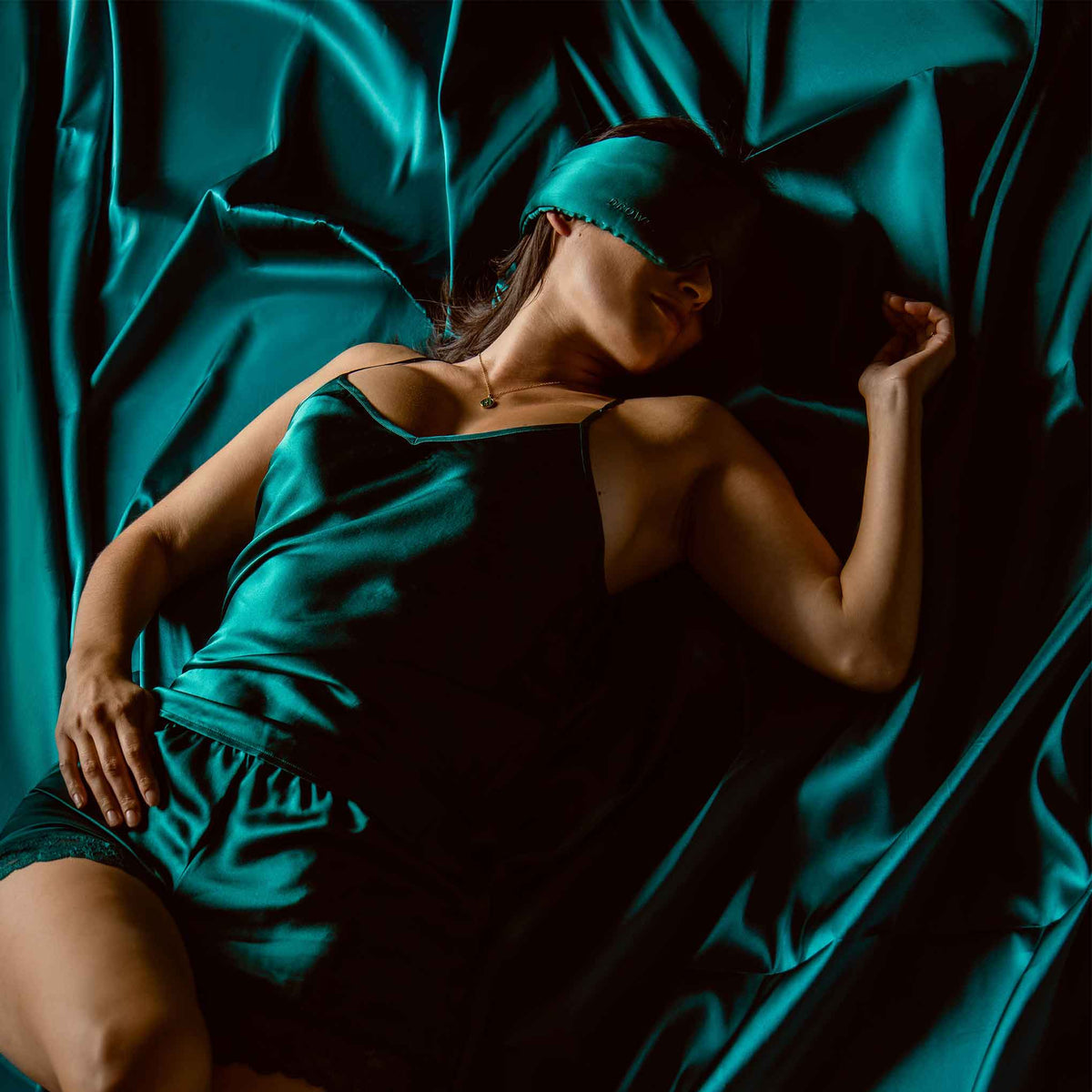 Model sleeping on green silk with Drowsy Silk Sleep Mask