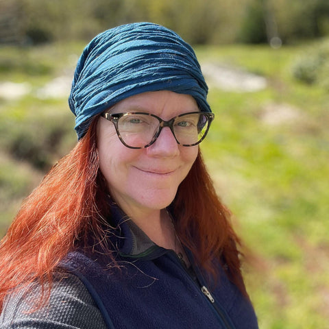 image shows woman artist with red hair and blue hat in a green field