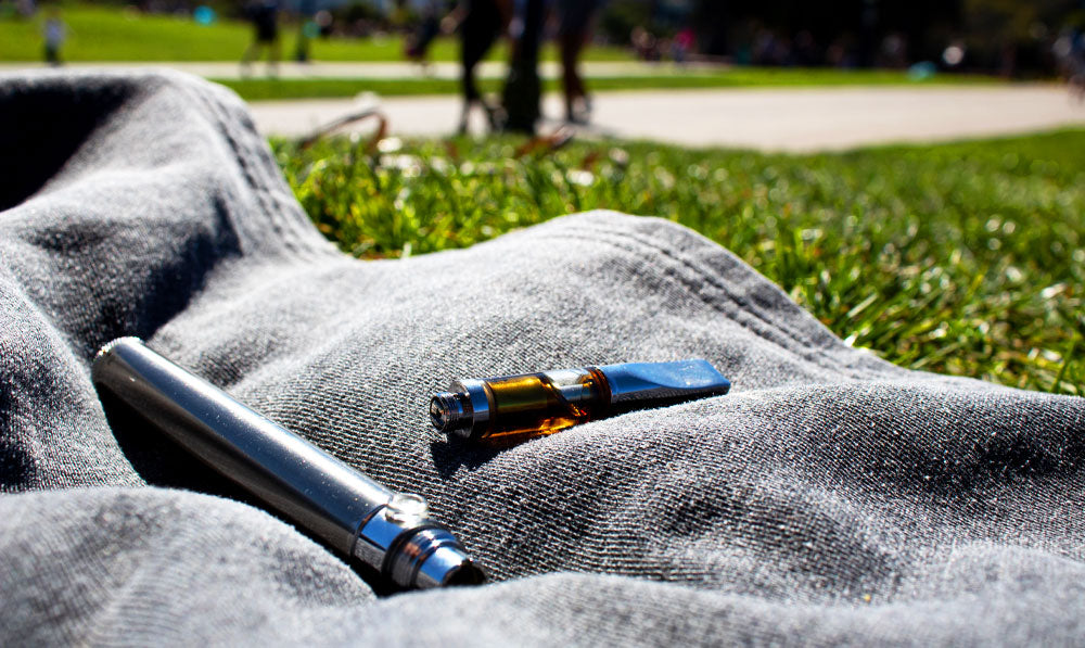 Vape and cartridge resting on jean jacket out in the sun