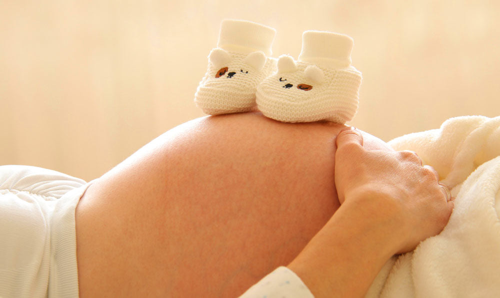 Pregnant woman laying down with baby booties resting on top of her belly