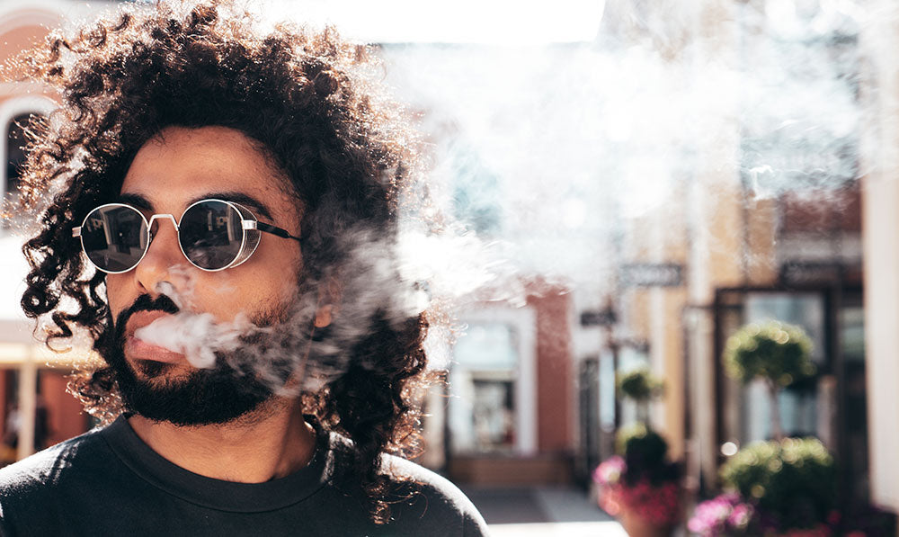 Latin man with curly hair vaping outside