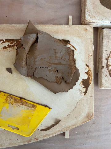 Image of dried clay being scraped off a plaster batt.