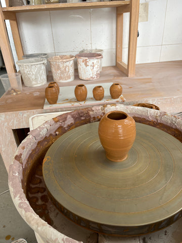 Image of small thrown pot sitting upon a pottery wheel head.