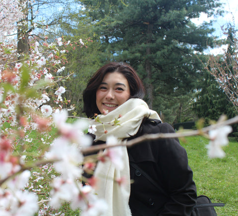 young asian woman smiling and standing next to flowers outdoors