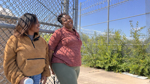 Two Black Women Talking and Smiling in Front of Fence