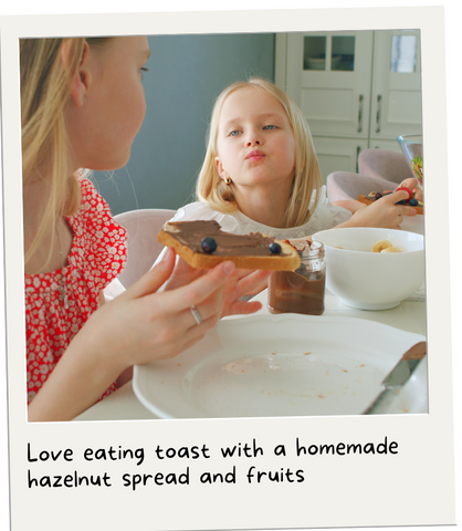 A polaroid of two girls enjoying toast with hazelnut spread and fruits. 