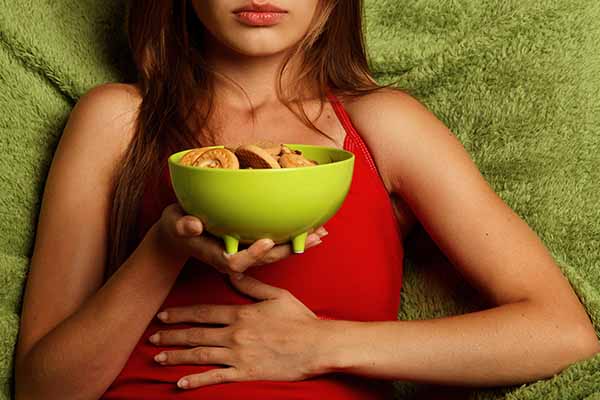 Woman holds her stomach as she displays a bowl of nutritious food