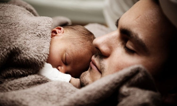 Photo of a man napping with a little baby sleeping on his chest.