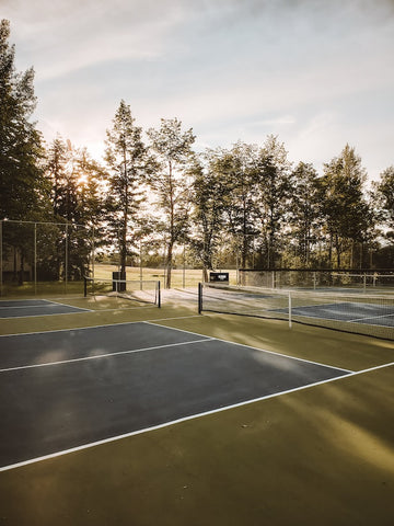 a shady tennis court surrounded by trees