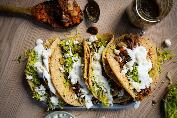 Plate of tacos de picadillo, topped with queso fresco, salsa, and lettuce