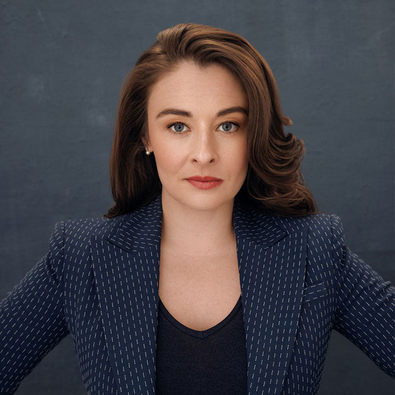 A headshot of Kaytlin Bailey wearing a blue blazer in front of a dark blue background.