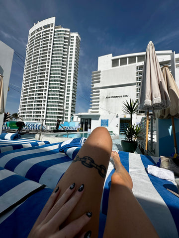 Braelinn Frank's legs with a chainlink tattoo on a striped loungechair in Miami with tall buildings in the background.