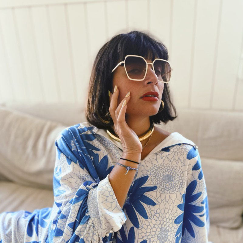 A headshot of Arielle Egozi in a blue and white shirt, sitting on a white couch.