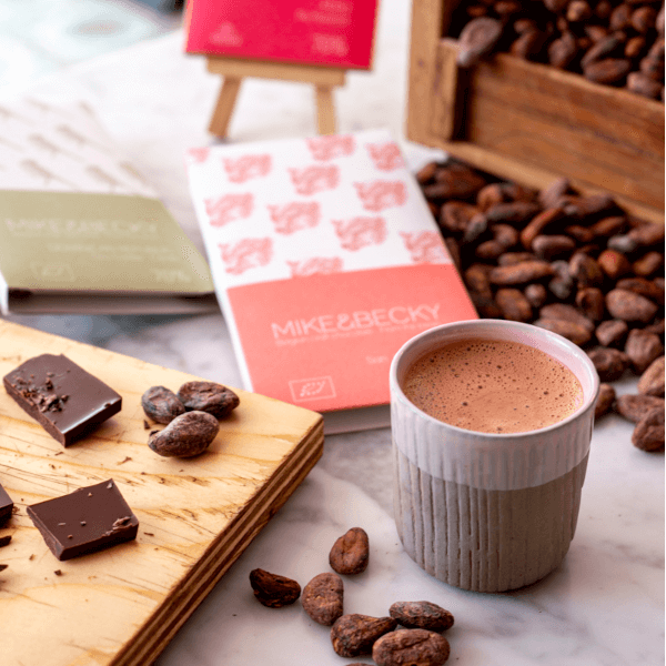 Eine Schokoladentafel liegt neben Kakaobohnen und einem Glas Trinkschokolade