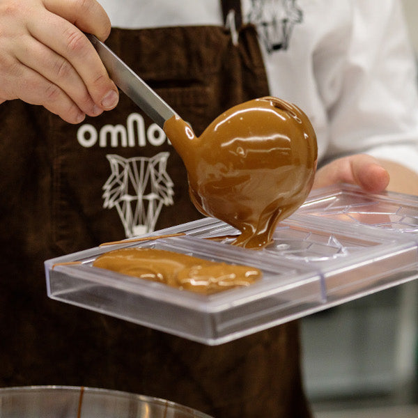 Flüssige Omnom Schokolade wird mit Löffel in Form gegossen.