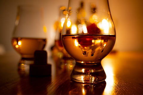 A glass of bourbon sitting on a table with mood lighting behind