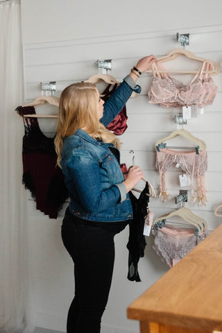 Owner touches pieces of pink lace lingerie on display wall | Society Lingerie - Canadian Lingerie Boutique