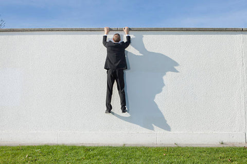 man hanging by his hands from the top of a wall