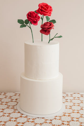 Trio of red crepe paper roses with three green leaves each sticking out of the top of a two-tiered white fondant wedding cake