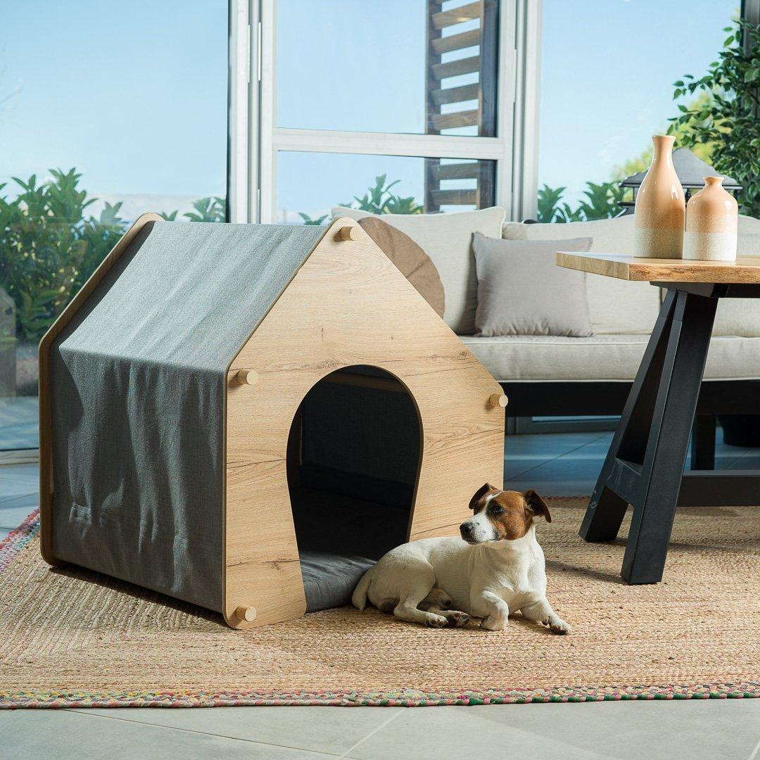 A small brown-white dog sits in his wooden dog house in the living room.