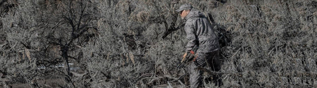 Man in brush hidden by camouflage hunting clothes