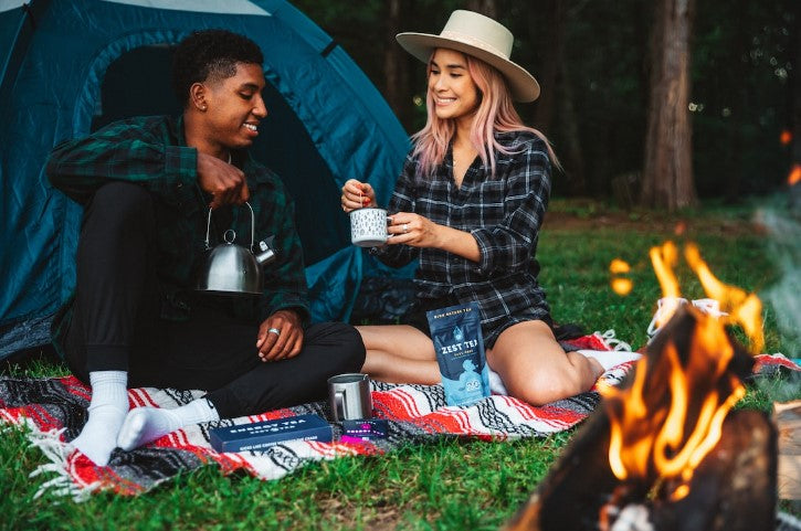 Mixed couple enjoying a cup of coffee over a camp fire