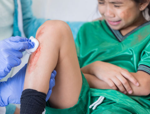Girl in football kit looking upset as medical professional tends to a cut on her shin