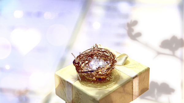 14kt gold trinket in the form of a birds nest sitting on top of a jewelry gift box