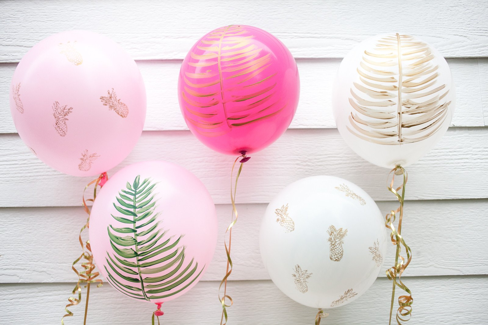 Three pink and two white coloured, printed balloons on a white wall.