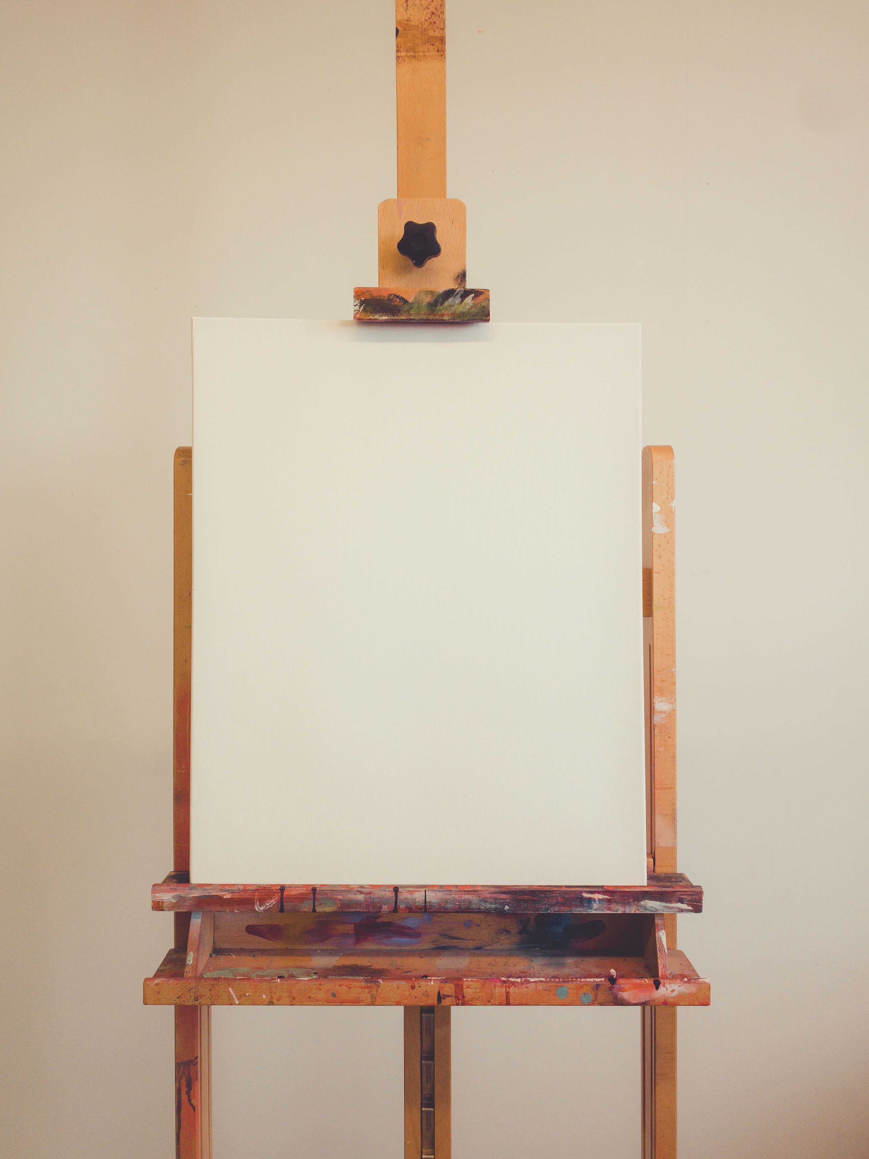A wooden easel with a blank empty canvas sitting on it in a room with white walls.