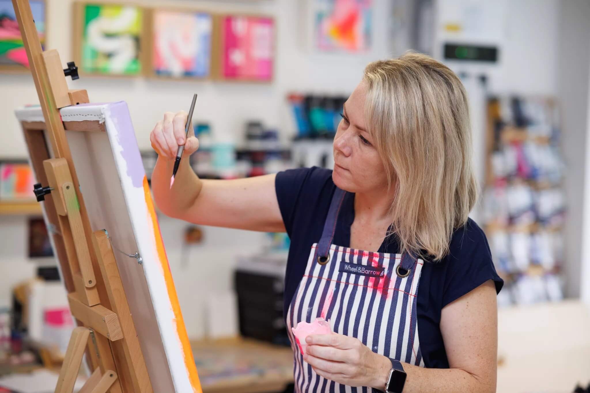 Michelle holding a paintbrush with pink acrylic paint painting a canvas.