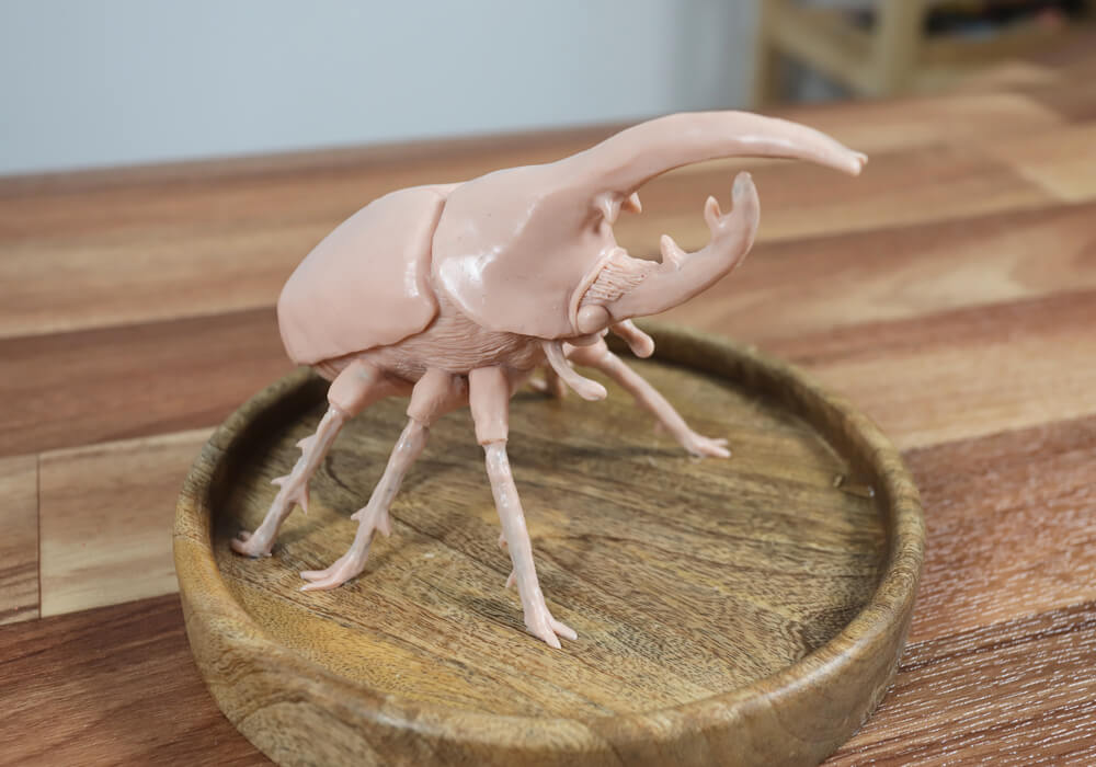 A polymer clay beetle sculpture sitting on a wooden place mat on a wooden table.