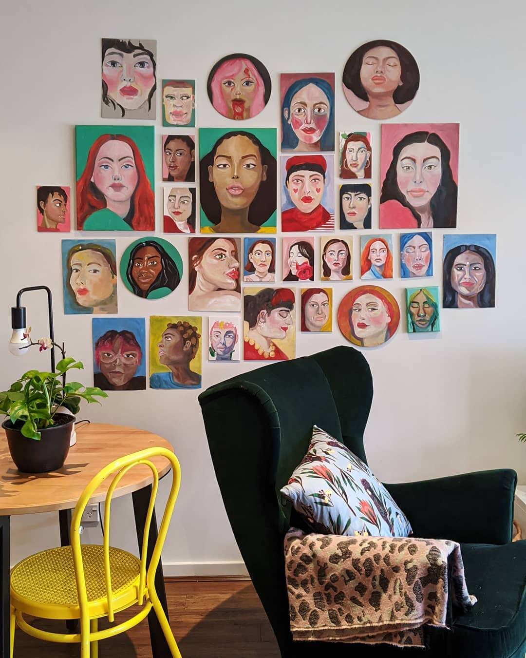 Colourful abstract portraits on a wall near a bright yellow chair and a green arm chair.