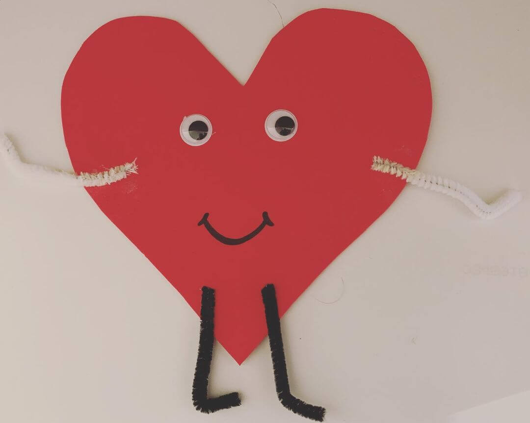 Smiling love heart made from cardboard with googly eyes and arms.