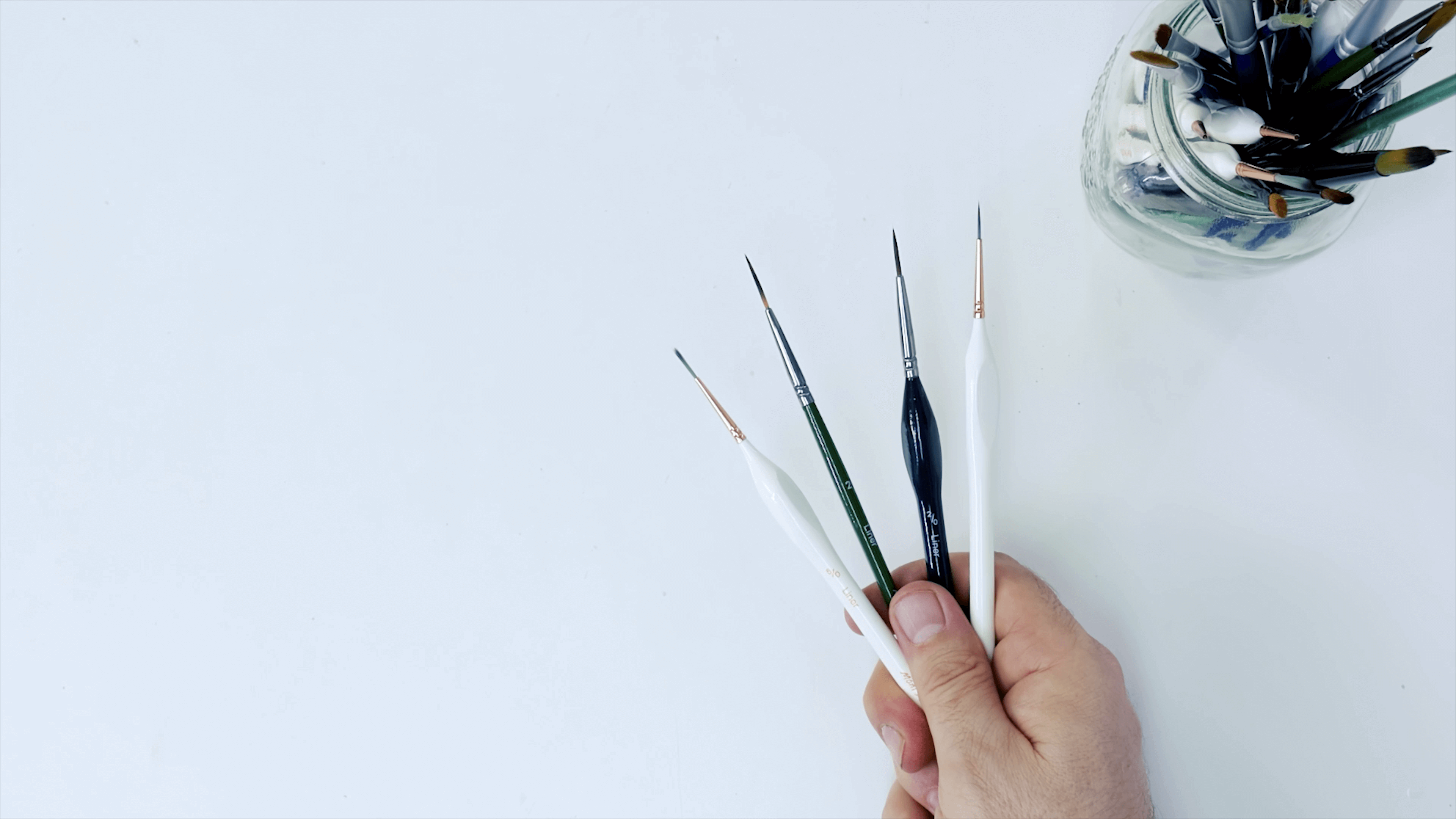 Hand holding four different sizes of liner paint brush.