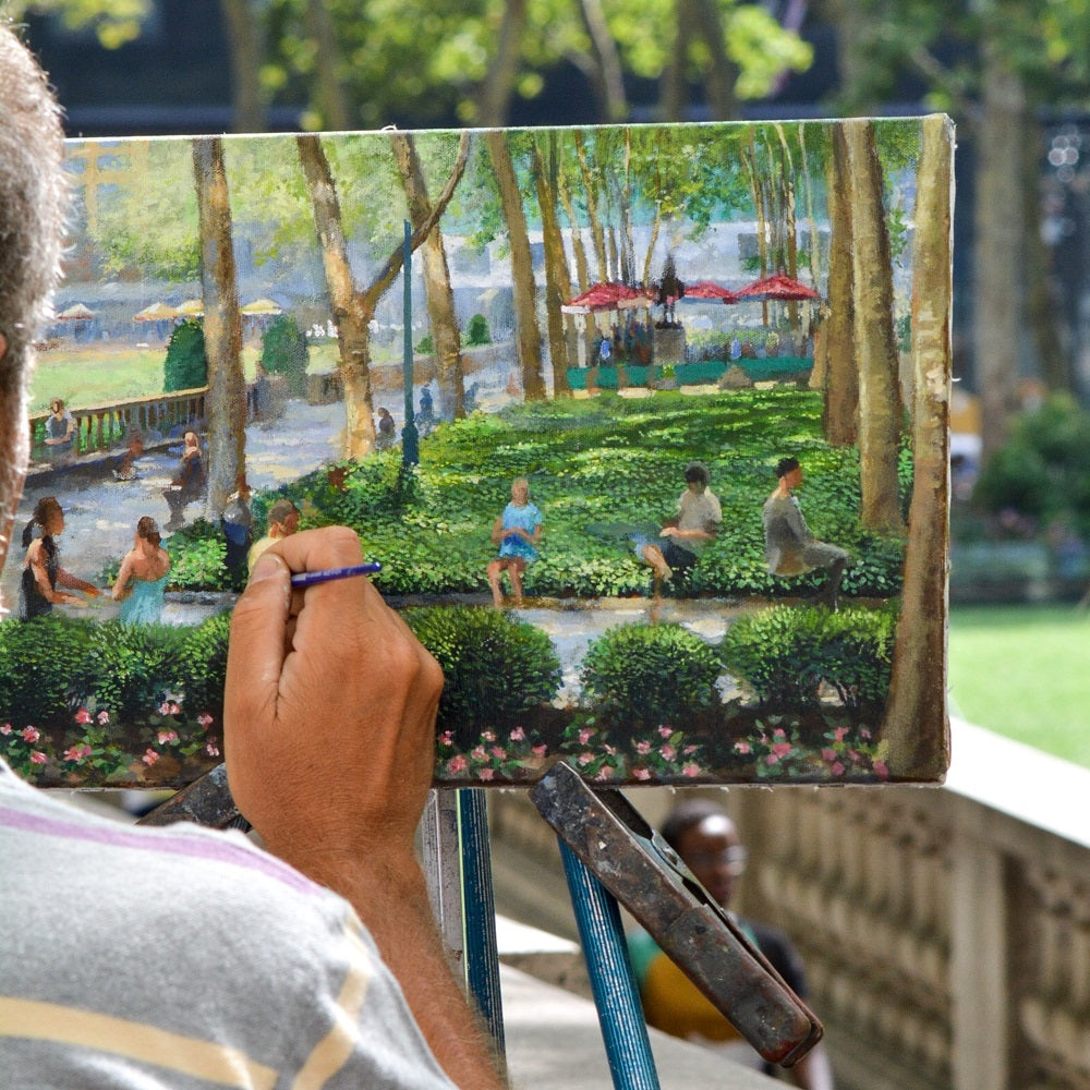 Man paints a busy park outdoors on easel which shows the outdoors behind.