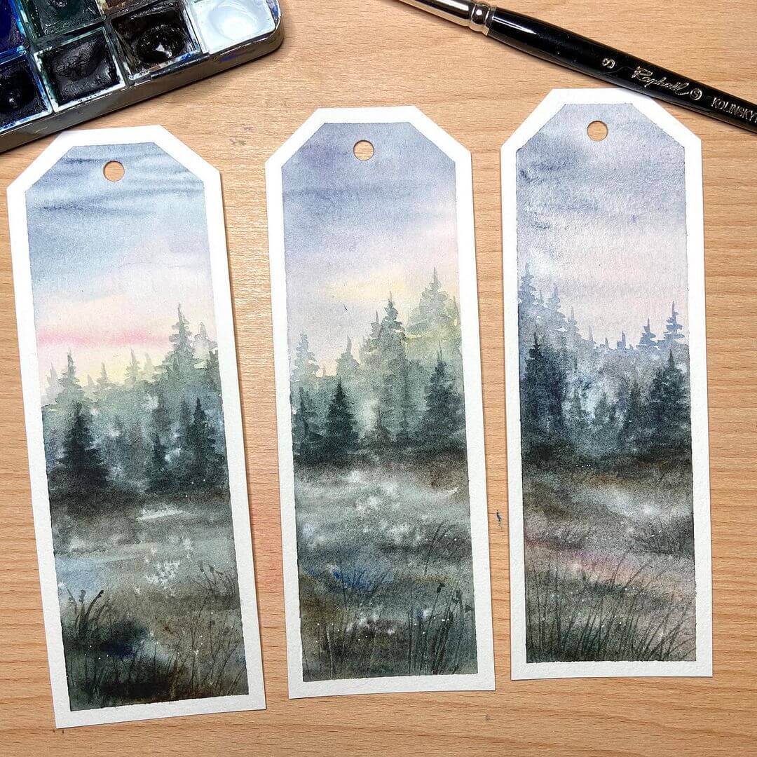 Three bookmarks on a table with watercolour brushes and pans near by.