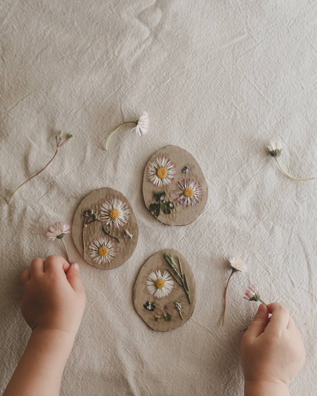 A child's hand pressing flowers into three circular clay moulds.