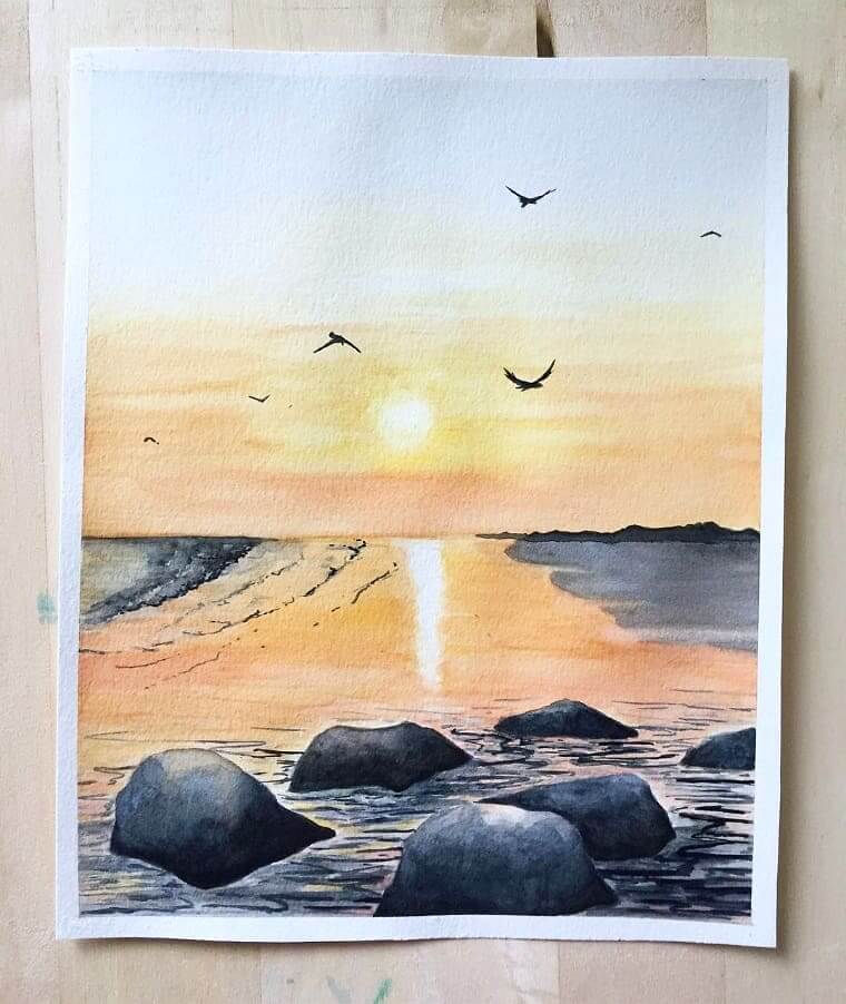 A sunrise watercolour artwork over Folley beach in California. Artwork is laying on a timber board.