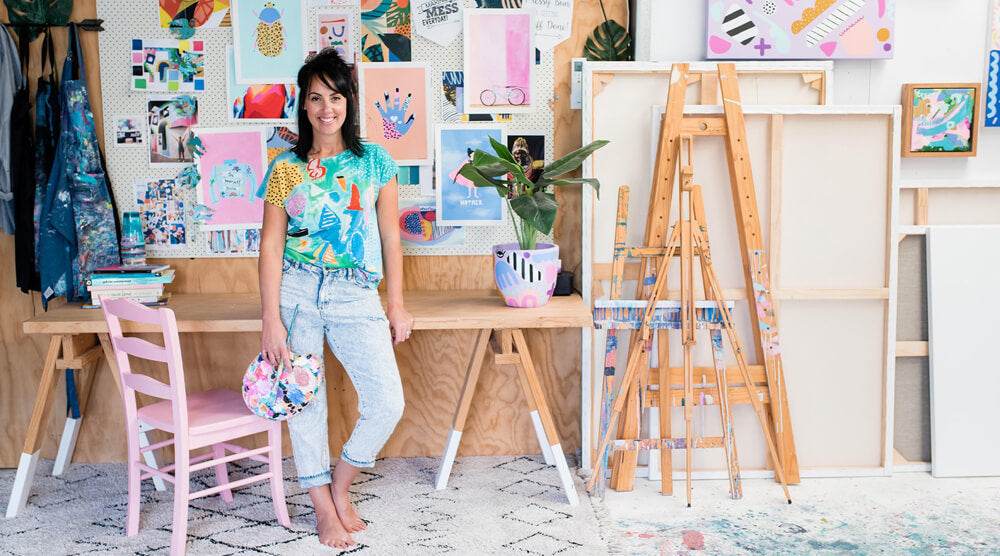 Deb McNaughton in studio holding paint palette next to a pink chair.