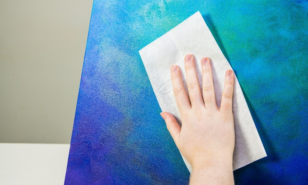 A hand cleaning the surface of a blue canvas.