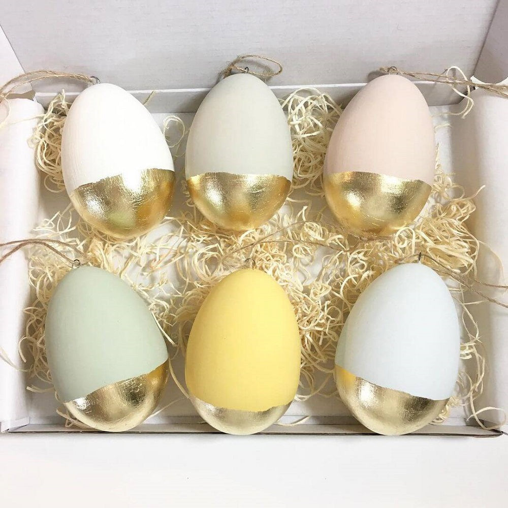 Four pastel coloured Easter eggs with gold leaf trim laying in a box.