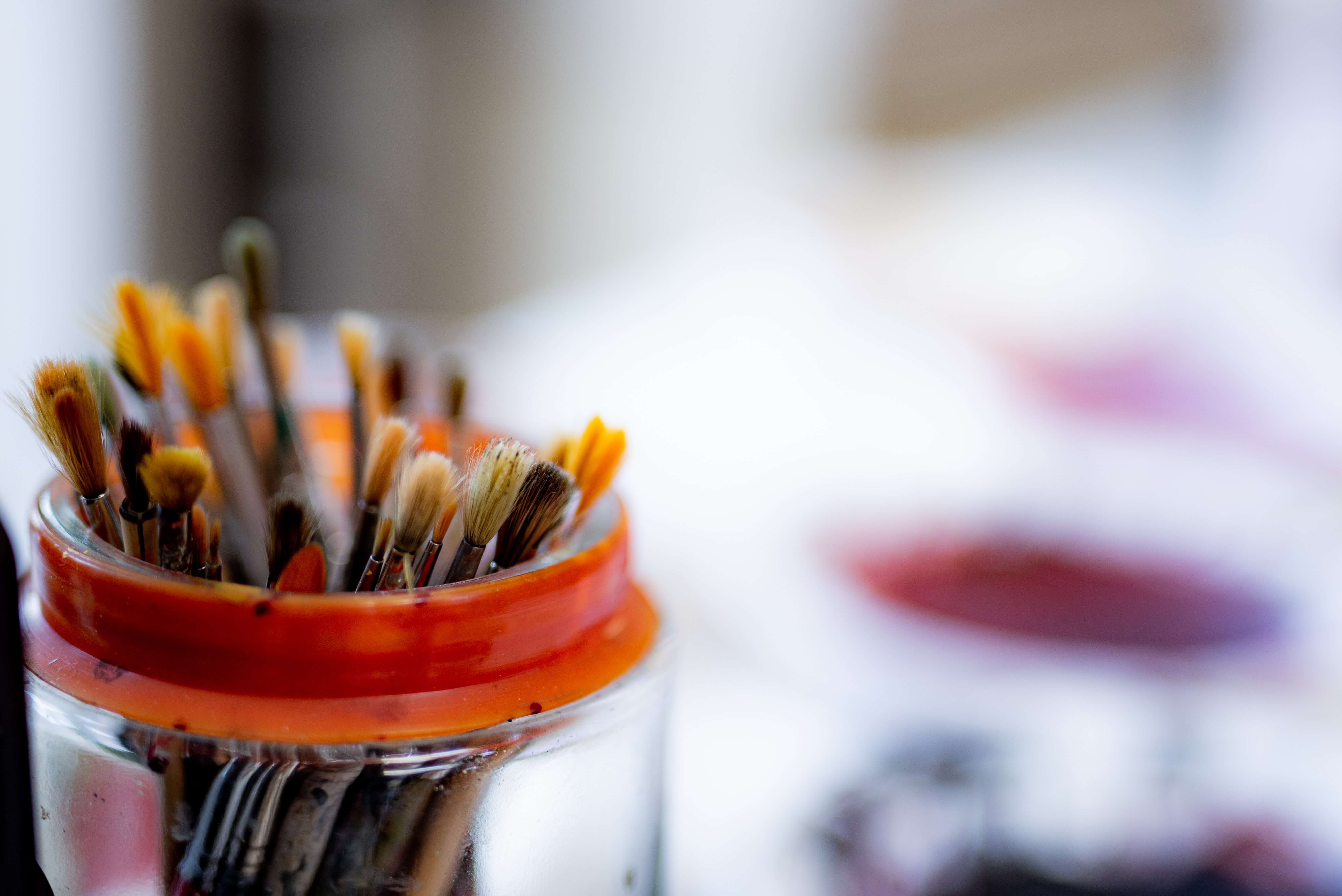 Shot of paint brushes standing in a jar with a red rim around the top and out of focus background.