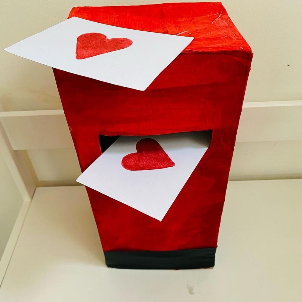 A cardboard box painted red like a mail box with two love letters inside and on top.