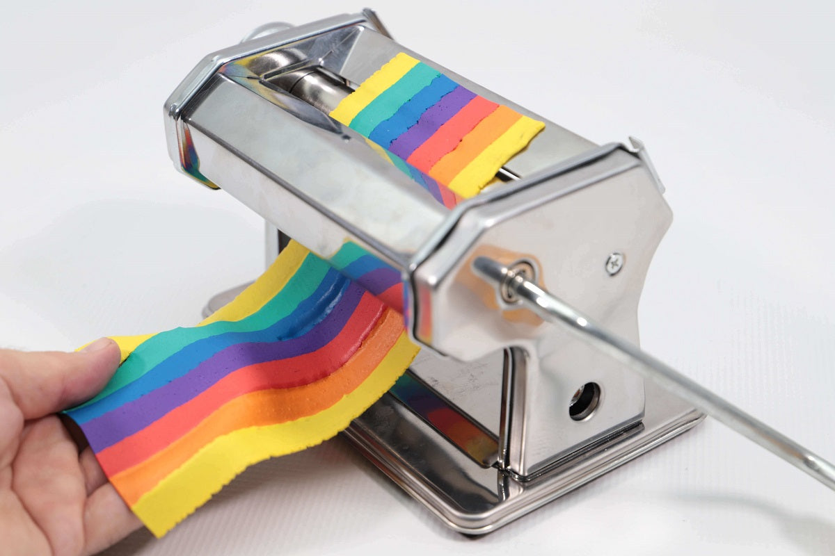 Strands of coloured clay being passed through a clay press by hand to create a rainbow sheet of polymer clay.